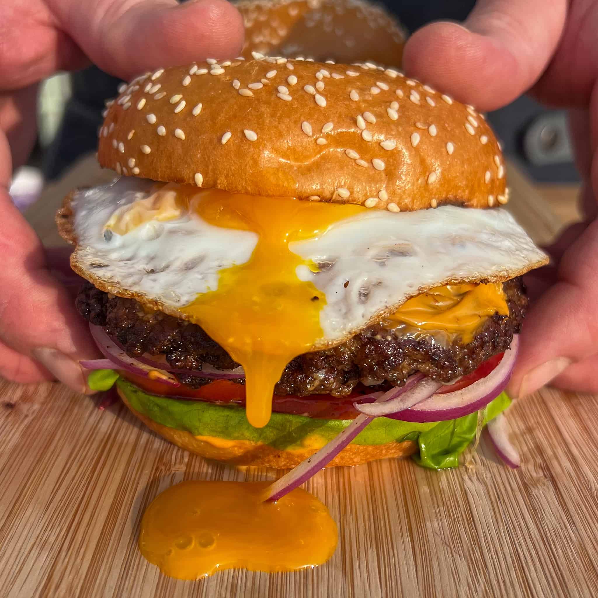 A burger with a sesame bun and an egg on the patty, with the burger also being topped with tomato, onion, and lettuce.