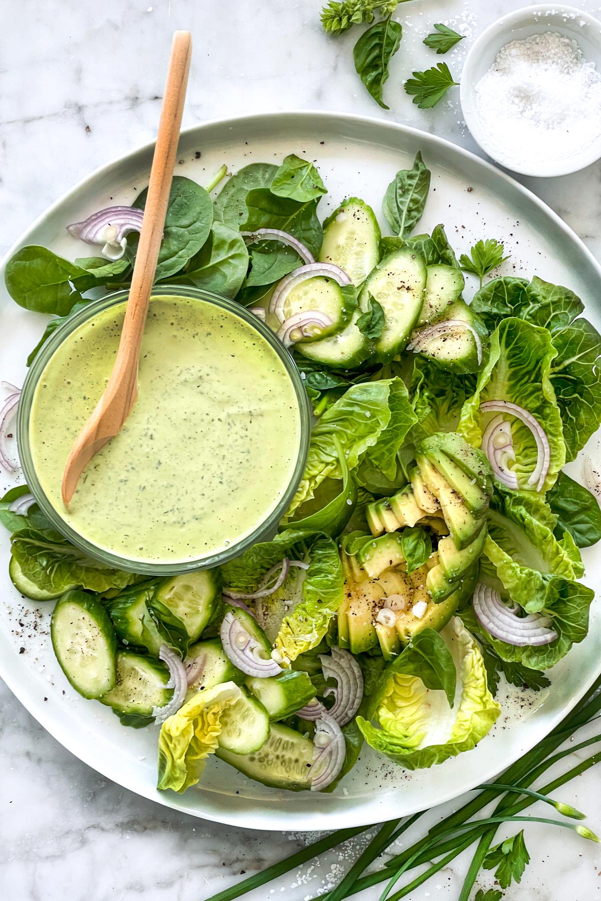 An image of a salad containing vegetables such as zucchinis and spinach, with a green dressing of some kind in a bowl with the salad.